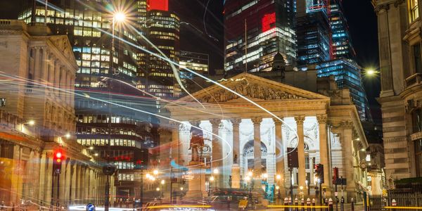 Nighttime cityscape with historic and modern buildings illuminated with light trails from traffic.