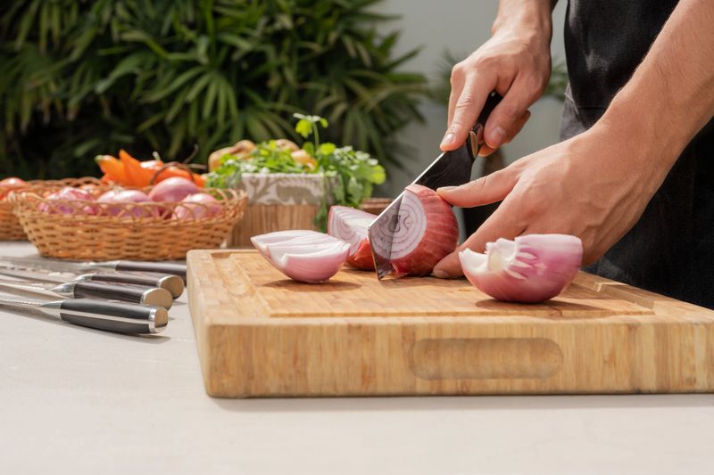 Close up view of the hands of a man chopping onions in a table in a garden