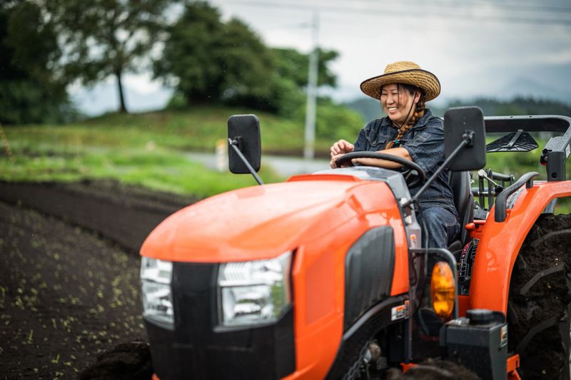 A mid age Japanese female farm worker operating a farm tractor.