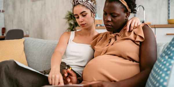 Two women sit closely, focusing on a paper together in a cozy living room.