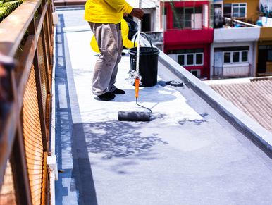A worker in yellow painting a rooftop with a roller brush.