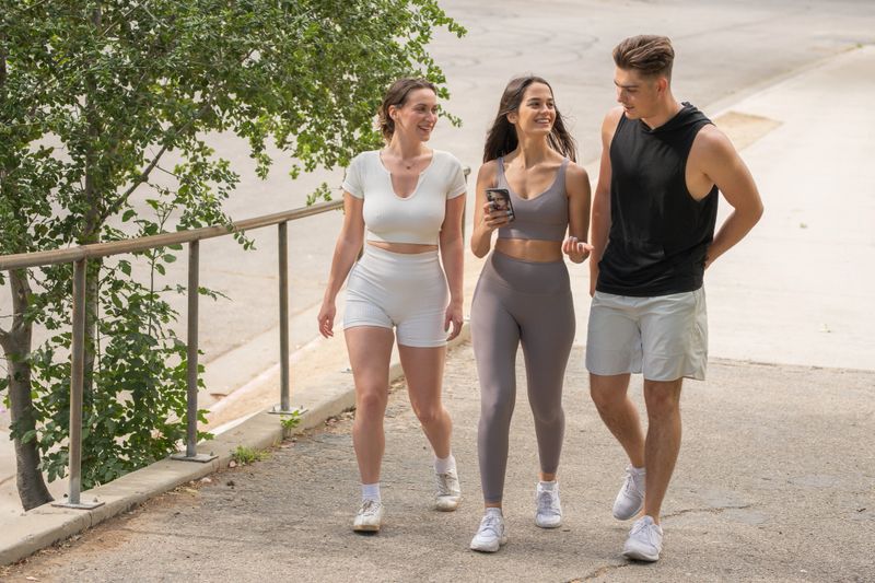 Three millennial-age friends in workout clothes chatting and walking in a park