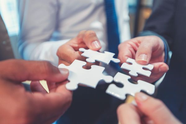 Four hands holding white puzzle pieces, symbolizing teamwork.