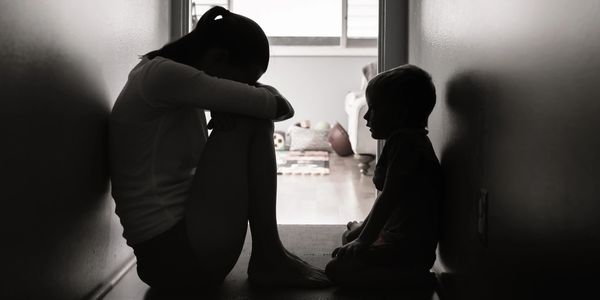 Silhouetted children sitting in a narrow hallway, facing each other in quiet contemplation.