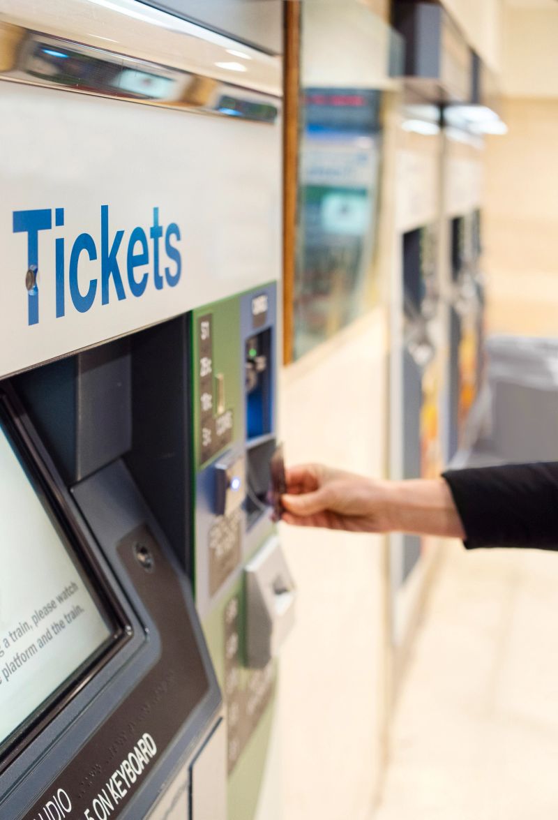 Close-up of a woman using a credit card to make a contactless payment for a train ticket at a station kiosk