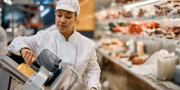 Retail deli employee wearing blue gloves sanitizing a meat slicer beside a digital thermometer  fres