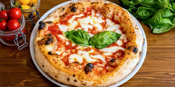 A classic Margherita pizza with fresh basil leaves on a white plate.