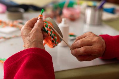 Hands weaving orange, white, and green threads.