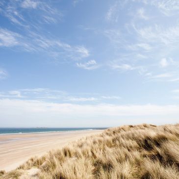 A beach with sand dunes and a partly cloudy sky.