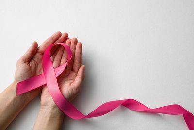 Hands holding a pink ribbon symbolizing breast cancer awareness.