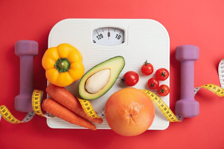 Healthy lifestyle essentials: dumbbells, fresh vegetables, fruits, and a weighing scale.