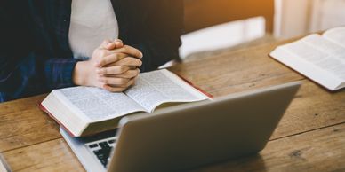 Hands folded in prayer in front of a computer