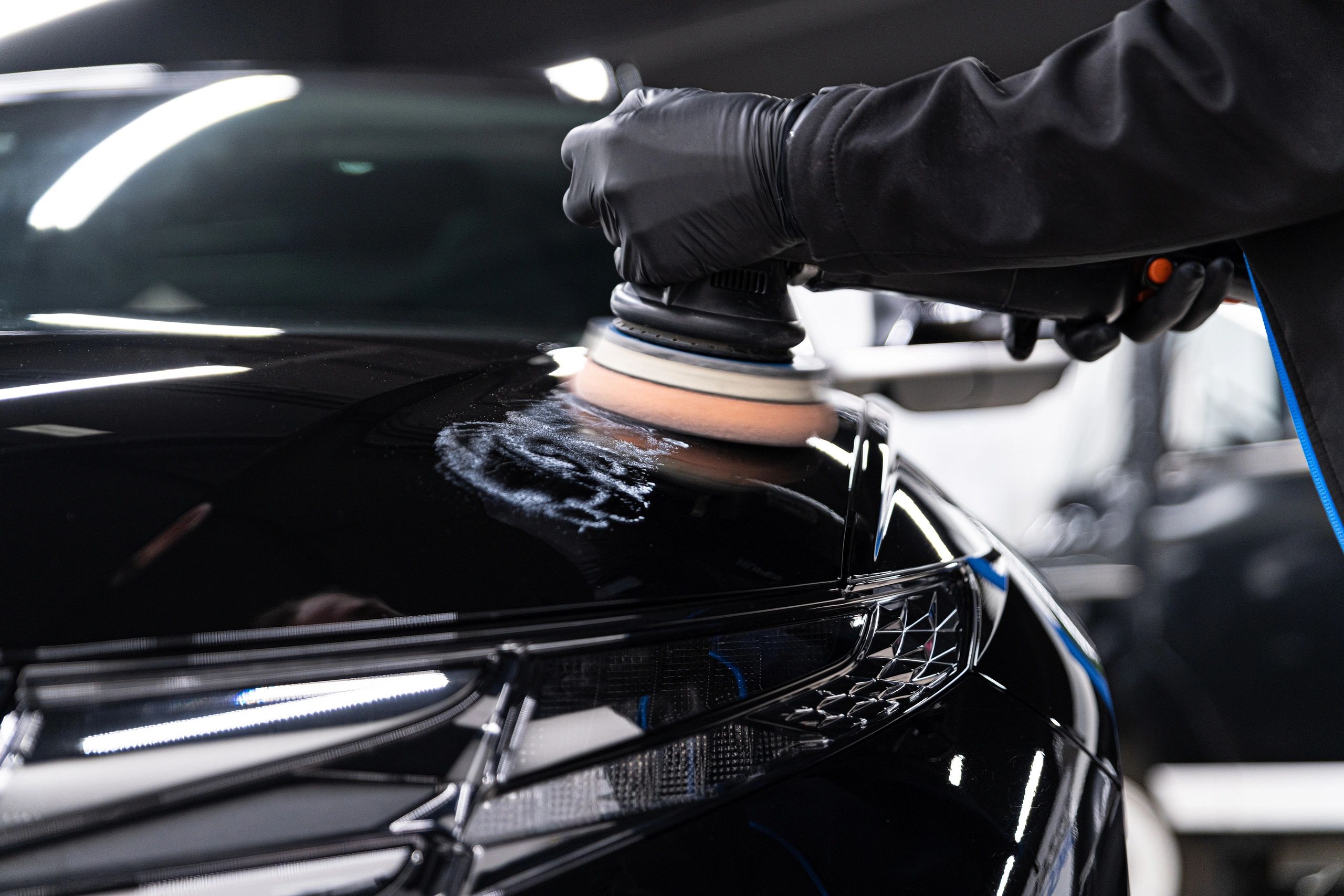 Person polishing a shiny black car surface with a buffer machine.
