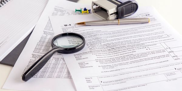 Magnifying glass over tax form with pen and stamp.