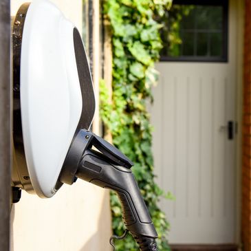 Electric vehicle charging at home with greenery and brick wall in background.