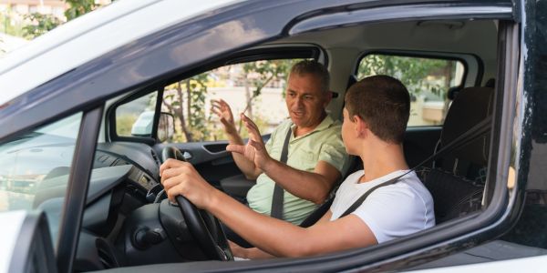 Man teaching teenager to drive in a car.