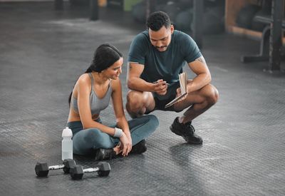 A fitness coach discusses workout progress with a seated woman at the gym.