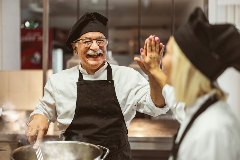 Team of cooks giving five with hands each other, while cooking in professional kitchen. Concept of teamwork and success at restaurant business
