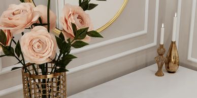 Elegant pink roses in a stylish gold vase on a white surface with gold candle holders.