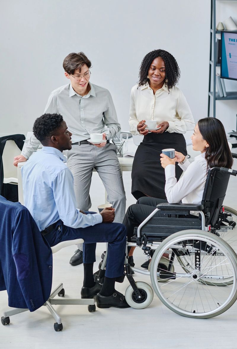 Group of young business people drinking coffee and talking to their colleague with disability at coffee break