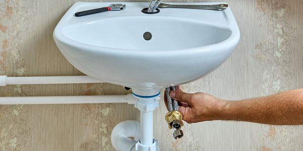 A person repairing a white sink with plumbing tools.