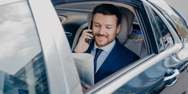 Businessman in a car talking on phone and reading newspaper.