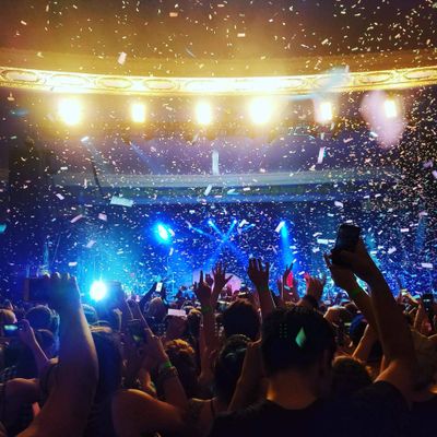 Crowd enjoying a vibrant concert with confetti and bright stage lights.