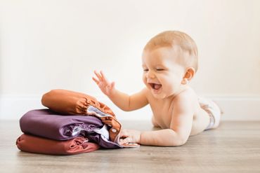 Happy baby playing with folded colorful clothes on the floor.