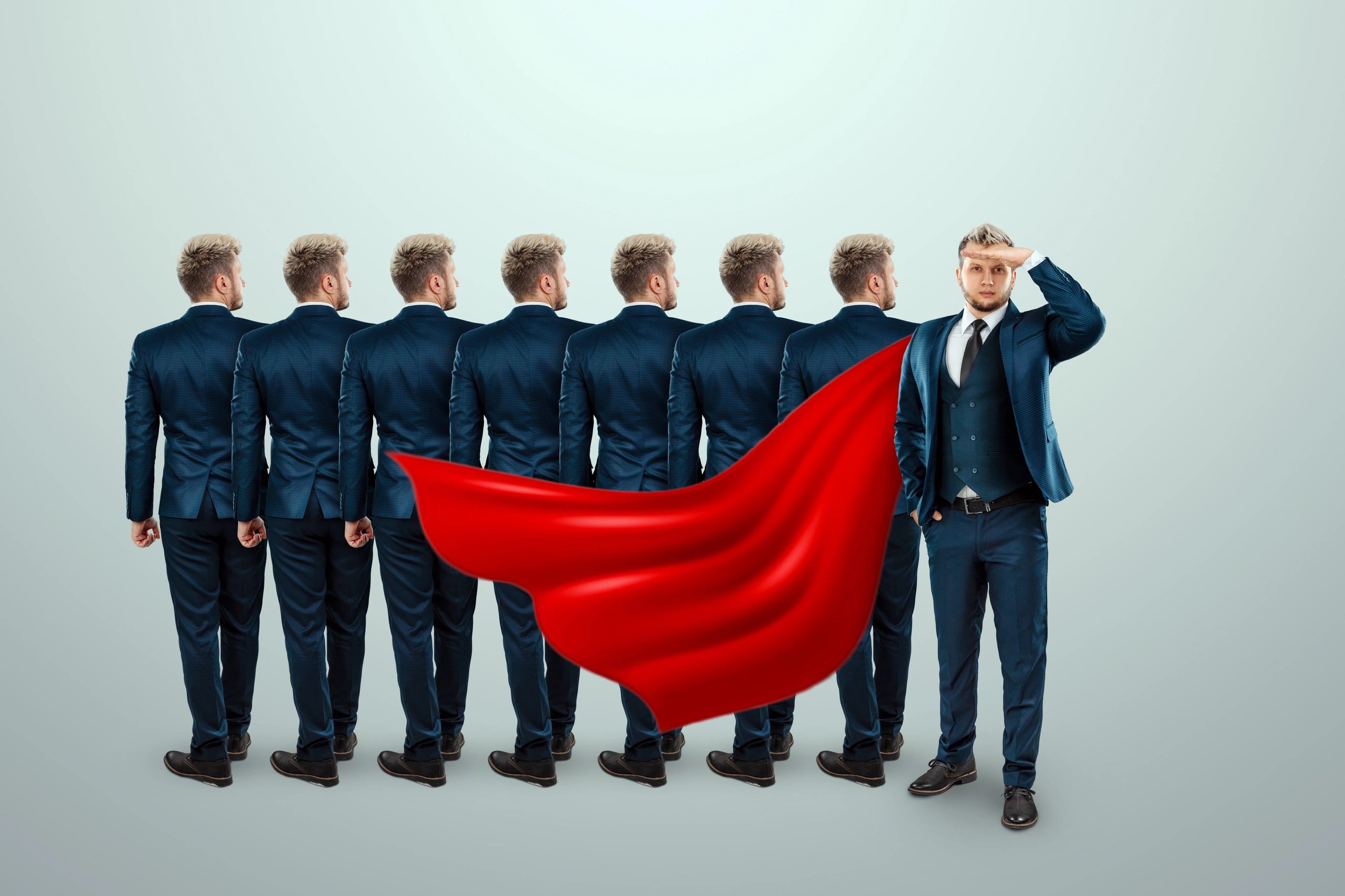 Man in suit with red superhero cape stands out from identical backs.