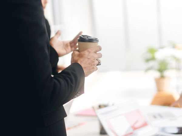 Person in a business suit holding a coffee cup during a meeting.