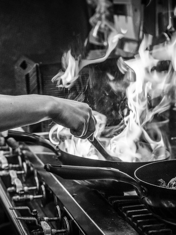 Hand cooking with flames on a stove.
