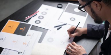 A person designing logos at a desk with sketches and drawings.