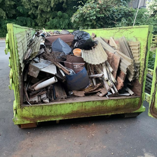 Une benne verte remplie de débris de construction et de sacs poubelles