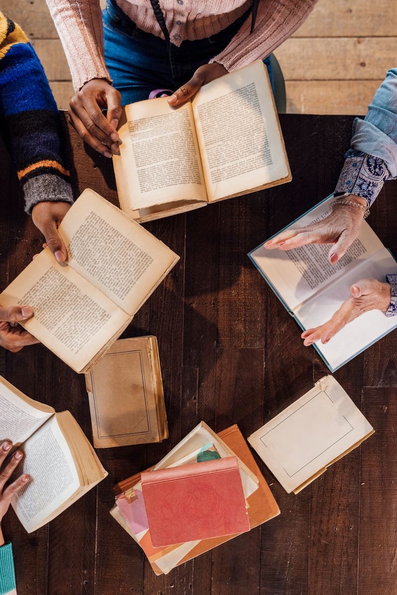 A medium, high-angle shot of an unrecognisable multiracial group of adults wearing casual clothing in a cafe in Newcastle Upon Tyne. They are at a book club, sitting around a table with books and talking.