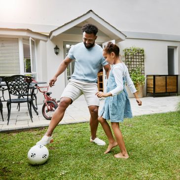 Father and daughter playing soccer together in the backyard.
