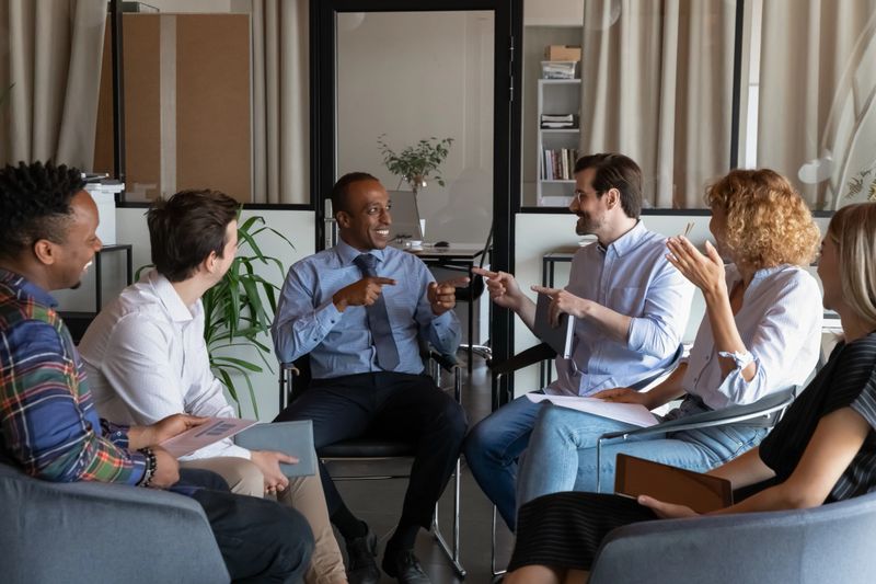 Focused diverse business people discussing ideas or problem solution, sitting in circle in comfortable armchairs in modern boardroom. Skilled mixed race employees involved in teambuilding activity.