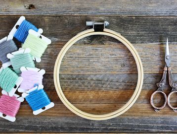 Embroidery supplies including colorful threads, wooden hoop, and vintage scissors on rustic wood.