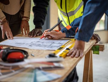 People collaborating on architectural plans at a construction site table.