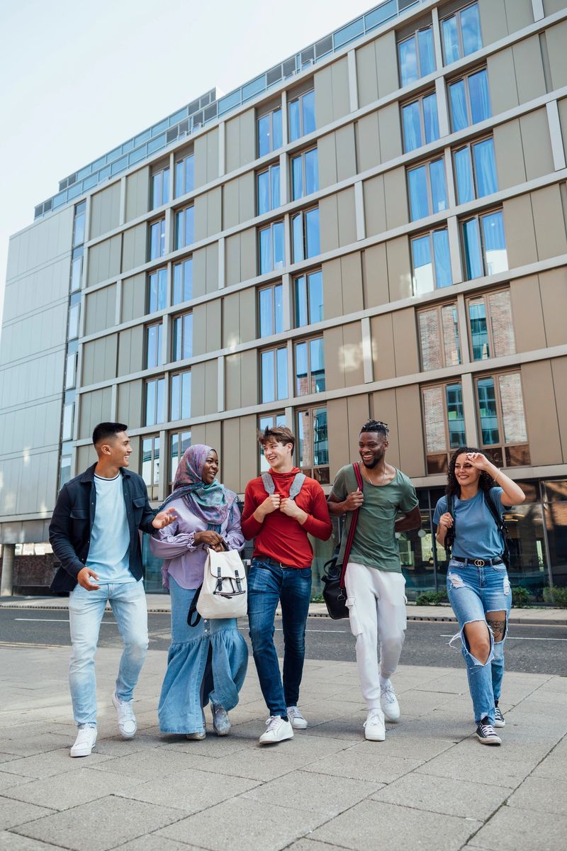 University students walking through the city centre of Newcastle upon Tyne, North East England with university accommodation behind them. They are laughing and talking with each other while they walk.