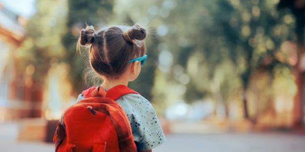 Little girl with a red backpack walking outside.