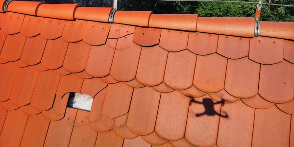 Shadow of a drone over damaged red roof tiles with a hole.