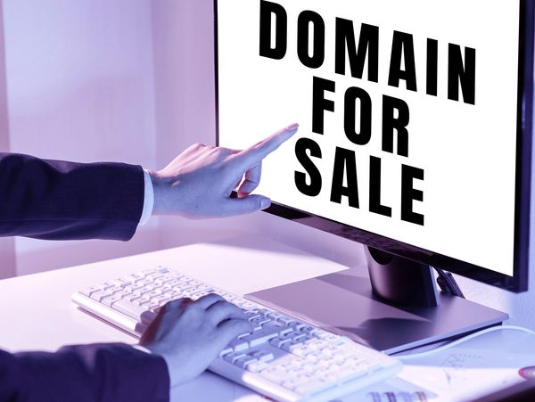 Person pointing at a screen displaying 'DOMAIN FOR SALE'.