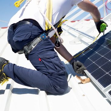 Worker installing solar panels on a rooftop while measuring dimensions.