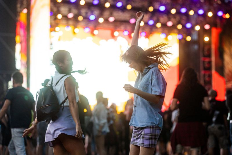Two girlfriends of Asian and Caucasian ethnicity are dancing in front of the stage and enjoying the atmosphere at a music festival.