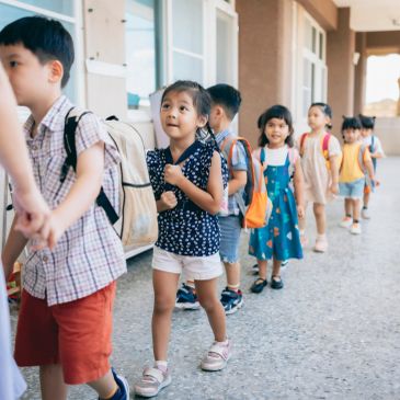 Children walking in a line at school, carrying backpacks.