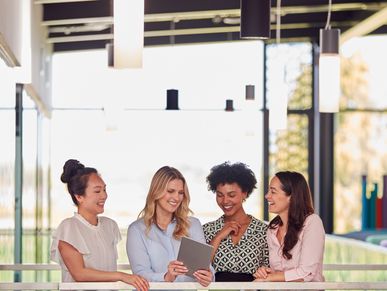 Four professional women smiling and looking at a digital tablet together.