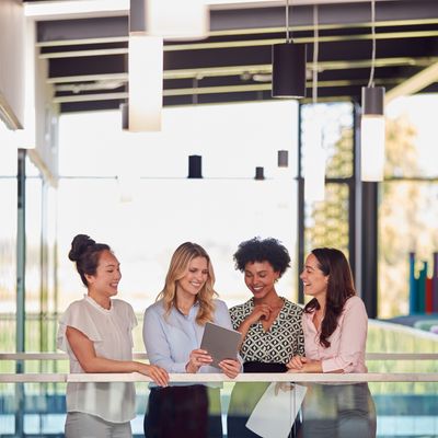 Four professional women smiling and looking at a digital tablet together.