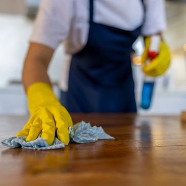 Person wearing yellow gloves cleaning a wooden table with a cloth.