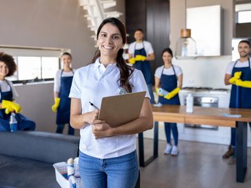 Smiling cleaning supervisor with clipboard and team in a modern home.