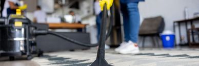 Smiling woman in orange gloves with cleaning supplies pointing up.